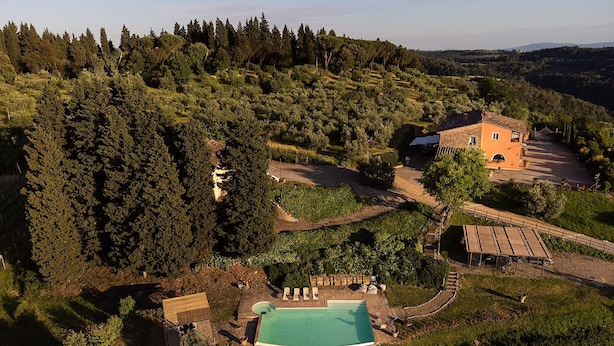 An aerial view of a property with a swimming pool, a large house, and surrounding forested hills.