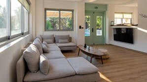 Un soggiorno moderno con un divano componibile, un tavolino da caffè e una televisione. Sono presenti ampie finestre e una porta che dà sull'esterno.