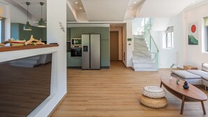 Una cucina moderna con forno integrato e un grande frigorifero, una scala che conduce a un piano superiore e una zona pranzo con tavolo in legno e cuscini.