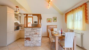 A kitchen with a stone island, wooden cabinets, a dining table with chairs, and a window with curtains. - Villa Ulika by Villas Guide (Vodnjan)