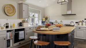 A modern kitchen with a central island, bar stools, a coffee maker, and various food items. - Beautifully presented spacious holiday cottage - Gardeners Cottage (Brockhampton)