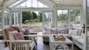 A conservatory with a glass roof, furnished with sofas and chairs, and a view of a garden. - Beautifully presented spacious holiday cottage - Gardeners Cottage (Brockhampton)
