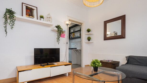 Een moderne woonkamer met een flatscreen televisie, een glazen salontafel, een grijze bank en een witte tv-meubel.