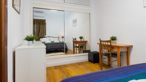 Een slaapkamer met een bed, een bureau, een stoel, een klein tafeltje en een spiegel.