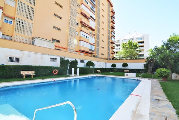 Uma piscina cercada por um edifício com varandas e um arbusto.