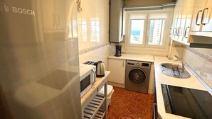 Een compacte keuken met een Bosch koelkast, een wasmachine en een magnetron.