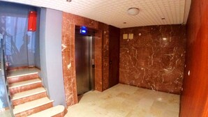 Een lobby met een marmeren vloer, een trap, een lift en een brandmelder.