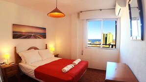 Hotelkamer met een bed, nachtkastje, lamp, raam met uitzicht en een klein tafeltje.