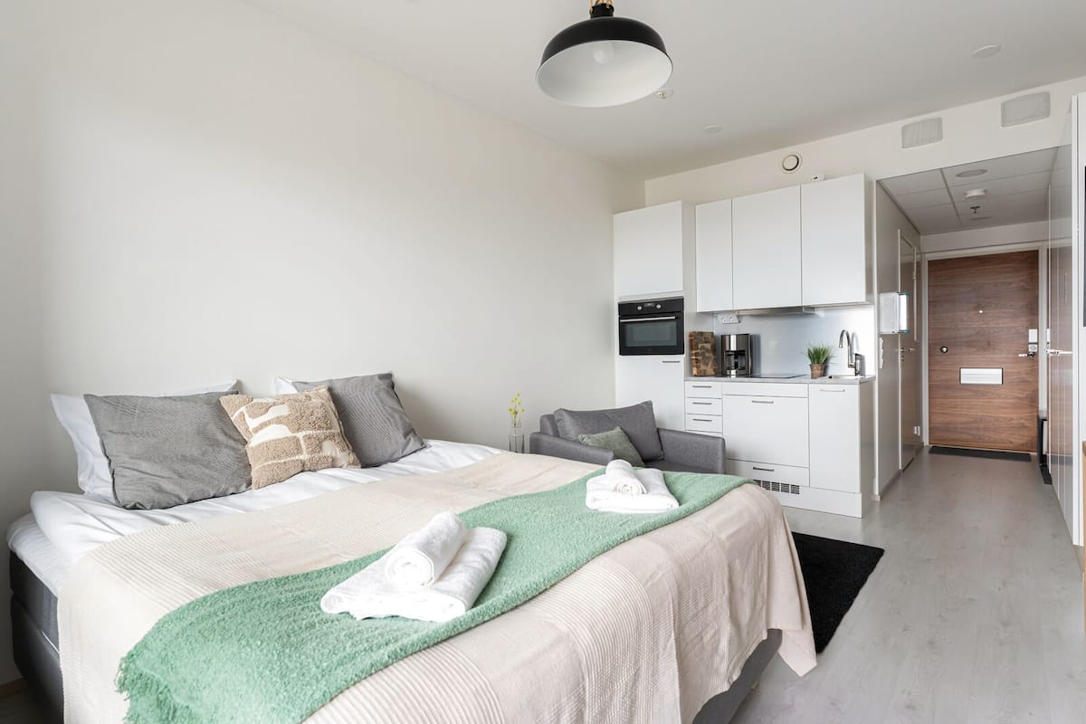 A modern hotel room with a bed, a green throw blanket, and a neatly made bed with towels.