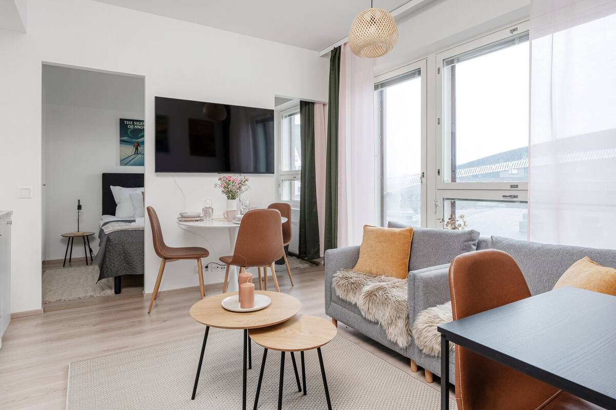 A modern living room with a grey sofa, brown chairs, a wooden coffee table, and a flat-screen TV mounted on the wall.