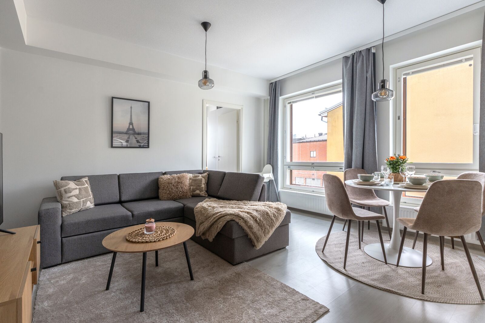 Ein modernes Wohnzimmer mit einem grauen Sofa, einem runden Couchtisch und einem Essbereich mit Tisch und Stühlen.