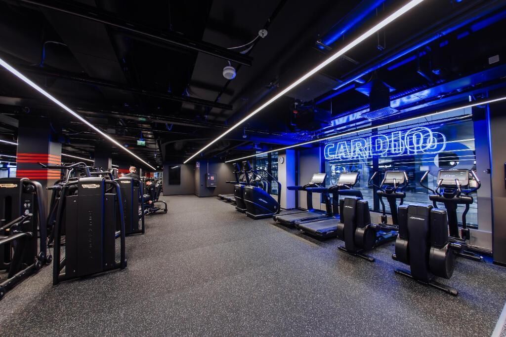Ein Fitnessraum mit Cardiogeräten und einer Neonreklame.
