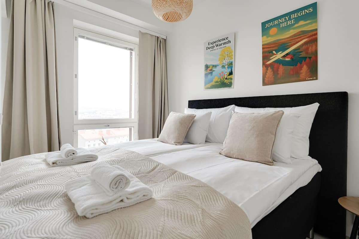 A hotel room with a large bed, a window with curtains, and two posters on the wall.