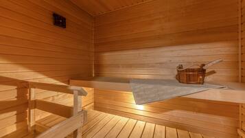 Una sauna con bancos de madera y un banco con una toalla y un cubo de madera.