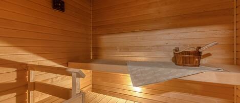 Una sauna con bancos de madera y un banco con una toalla y un cubo de madera.