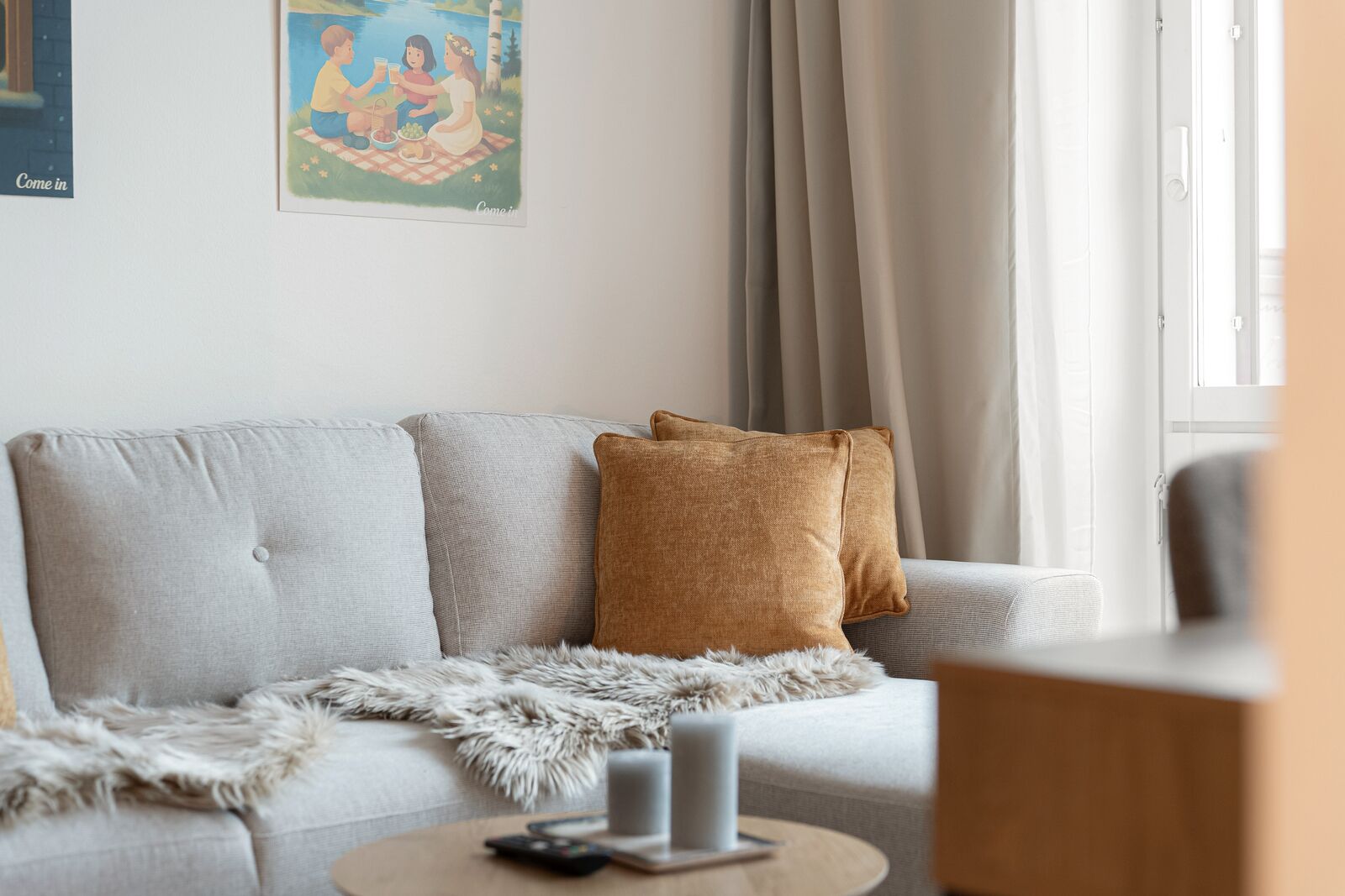 A living room with a sofa, a fluffy throw blanket, a remote control, and a candle on a side table.