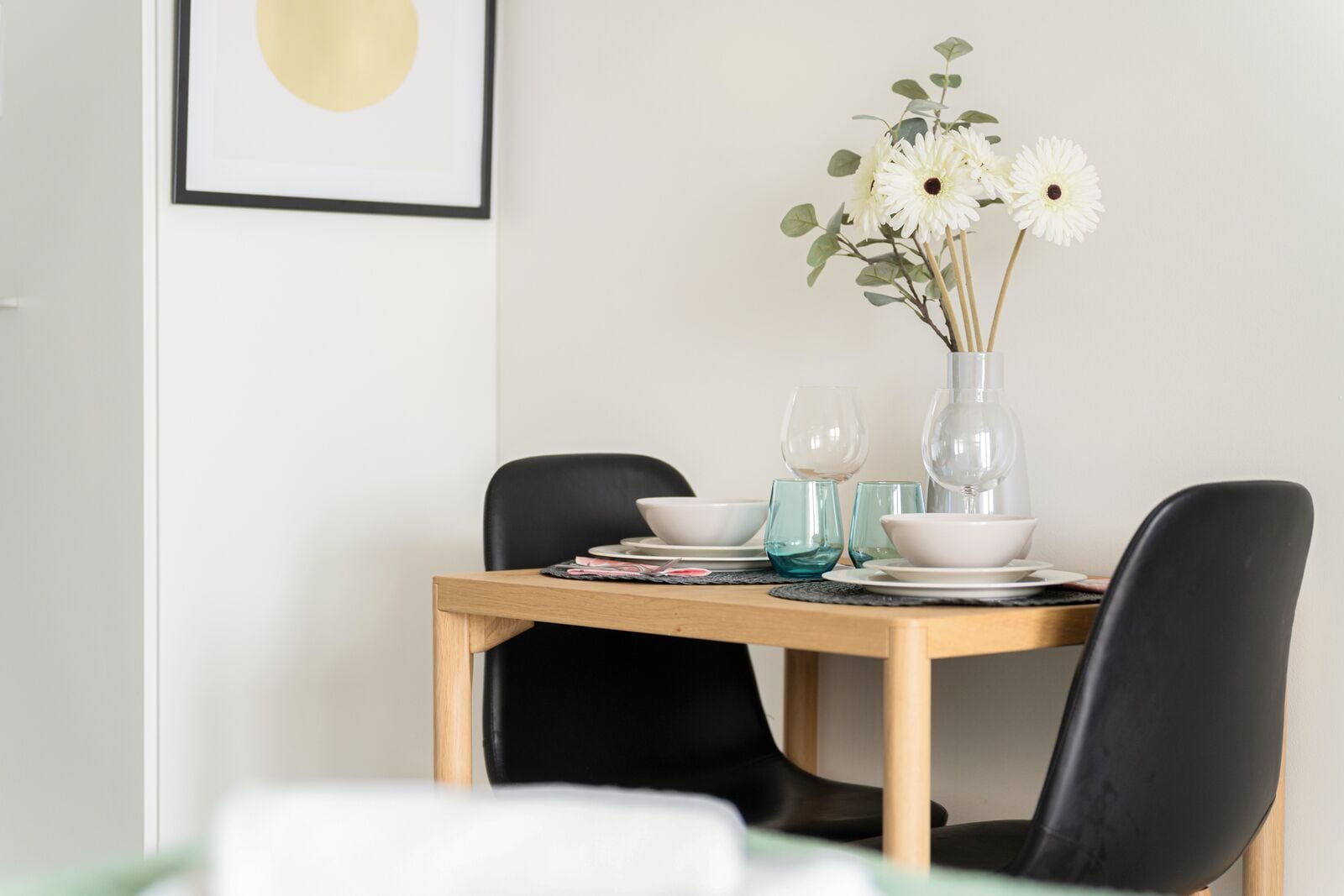 A dining table set with white bowls, clear glassware, and a vase with white flowers.