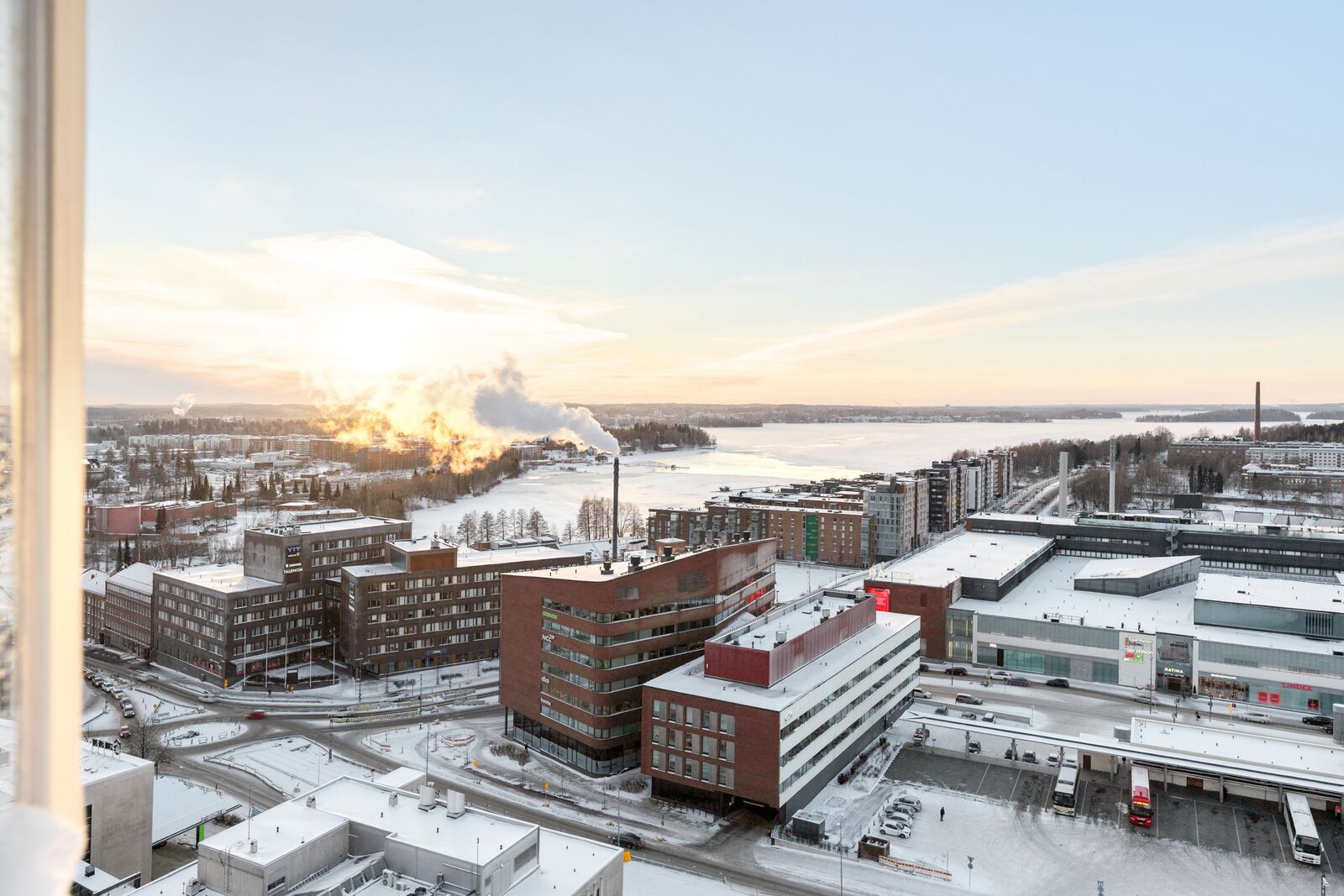 A cityscape with industrial buildings, a large factory with smoke stacks, and a river in the background.