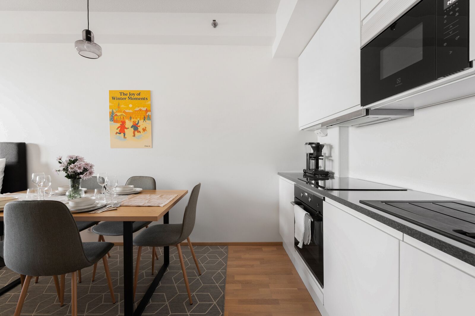 A modern kitchen with a microwave, coffee maker, and a dining area with chairs and a table set for two.