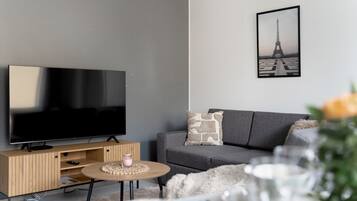 Una sala de estar moderna con un televisor de pantalla plana, un sofá gris, una mesa de centro de madera y un cuadro enmarcado de la Torre Eiffel en la pared.