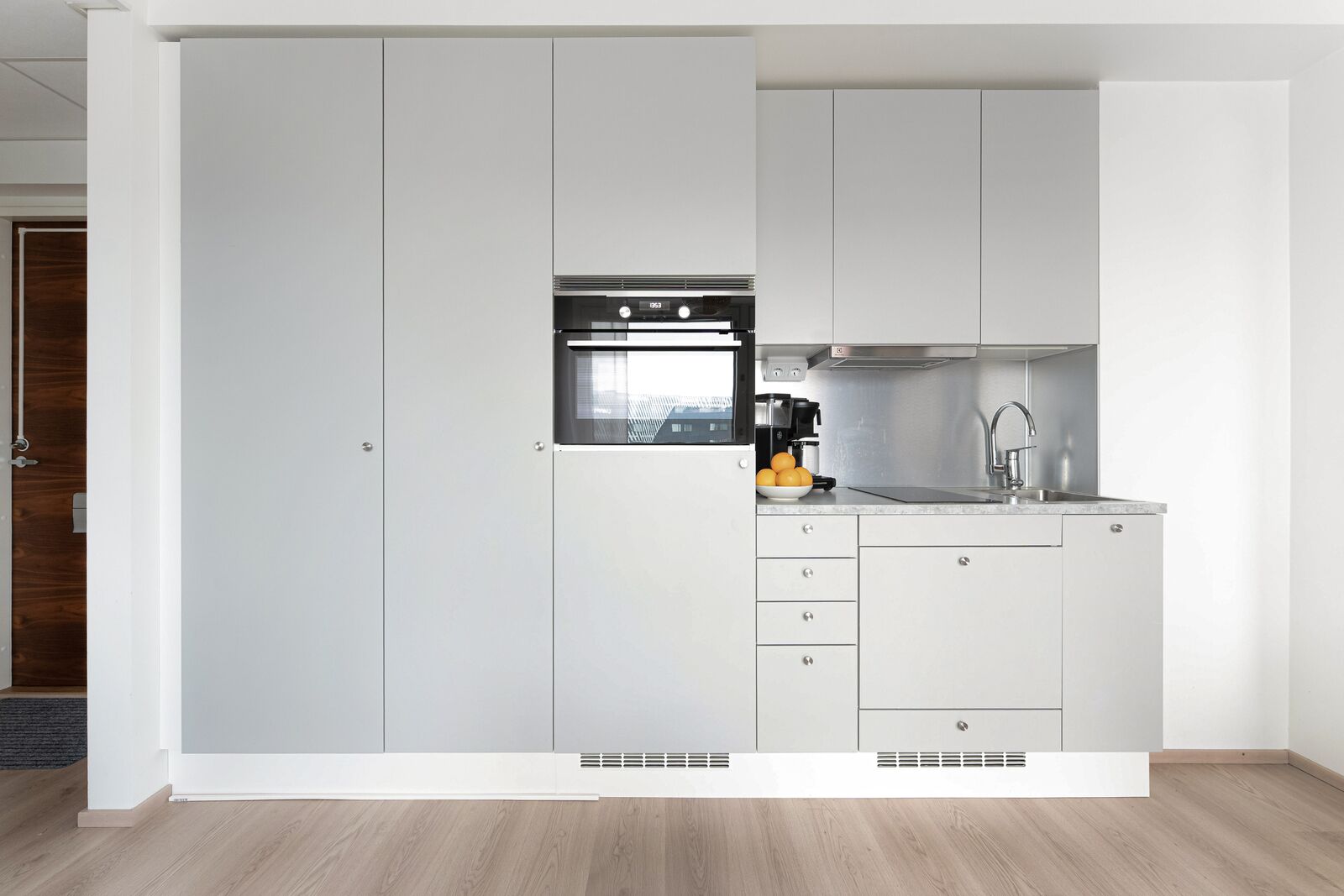 Una cocina moderna con armarios blancos, horno empotrado, cafetera y lavaplatos.