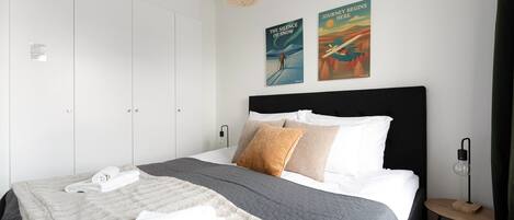 A modern bedroom with a large bed, white wardrobe, and two wall art pieces.