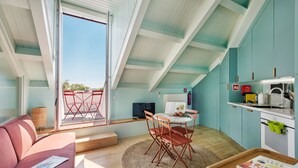 Een gezellige kamer met een bank, een eettafel met stoelen, een kitchenette en een groot raam met uitzicht.