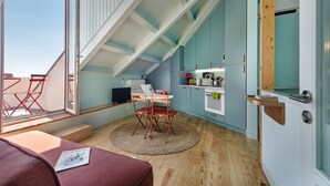 Een kleine keuken met een eethoek, houten vloeren en een uitzicht door een groot raam.