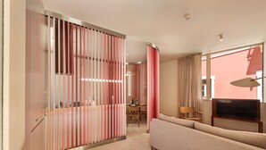 Ein modernes Hotelzimmer mit einem beigefarbenen Sofa, einem Fernseher und einem Essbereich mit Tisch und Stühlen.