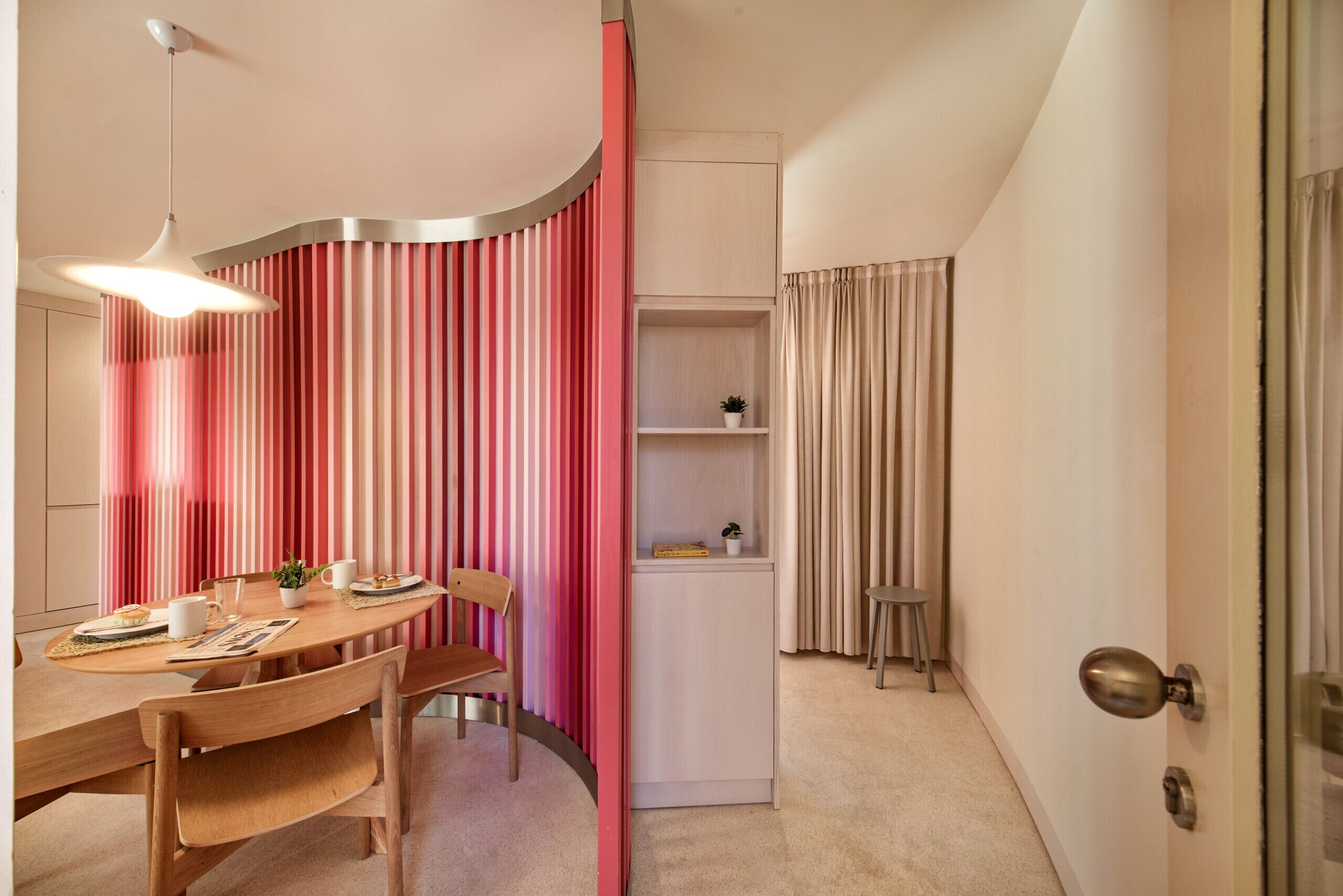 A dining area with a wooden table, chairs, a hanging light fixture, and a striped curtain.