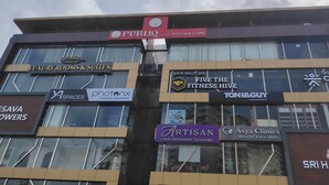 A multi-story building with various commercial establishments including a PUBLIQ KITCHEN & BAR, LUXURY ROOMS & SUITES, and ARTISAN CAFE | PATISSERIE | ACADEMY.