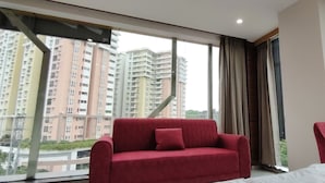A hotel room with a large window, a red sofa, a red armchair, and a bed.