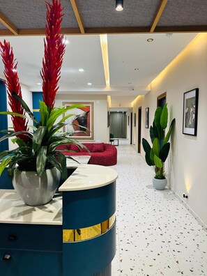 A reception area with a curved blue counter, potted plants, a red sofa, and a hallway with framed artwork and a terrazzo floor. - PubliQ Luxury Stays (Hyderabad)