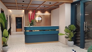 A reception area with a blue counter, potted plants, and a sign that reads "PUBQI stays".