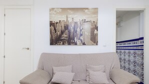A room with a checkered sofa, a cityscape painting, and patterned wallpaper. - Apartment 'Flat Near Macarena Basilica' with Wi-Fi and Air Conditioning (Seville)