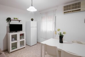 A small, clean room with a TV, refrigerator, dining table, and chairs. - Apartment 'Flat Near Macarena Basilica' with Wi-Fi and Air Conditioning (Seville)