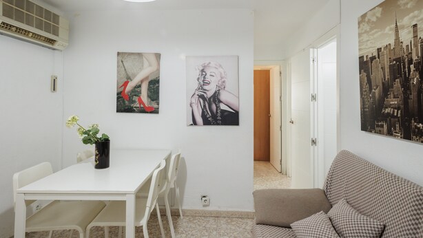 A dining area with a white table and chairs, a black vase with flowers, and two wall-mounted artworks depicting figures. - Apartment 'Flat Near Macarena Basilica' with Wi-Fi and Air Conditioning (Seville)