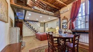 A dining area with a wooden table and chairs, a red patterned rug, and a staircase leading to an upper level.