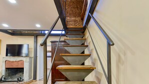 A spiral staircase with a brick wall at the top, a flat-screen TV on a mantelpiece, and a fireplace below.