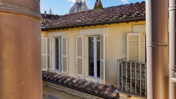 A building with a tiled roof, white shutters, and a balcony with a metal railing.