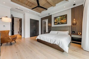 A modern bedroom with a large bed, wooden flooring, a ceiling fan, and a wall-mounted lamp. - SERENITY ON SUNRISE~Canal Front 5 BR/5.5 Ba New Town Home w/ Pool & Dockage! (Key West)