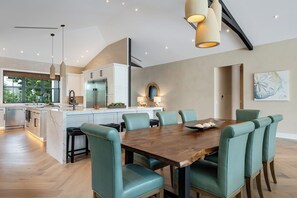 A modern kitchen with stainless steel appliances, a dining area with teal chairs, and a large window overlooking greenery. - SERENITY ON SUNRISE~Canal Front 5 BR/5.5 Ba New Town Home w/ Pool & Dockage! (Key West)