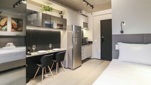 A modern hotel room with a bed, a desk with two chairs, a refrigerator, a microwave, and a small kitchen area. - ON Brooklin (Sao Paulo)