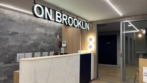 A reception desk with a sign reading "ON BROOKLIN" and a modern interior with a brick wall and wooden paneling. - ON Brooklin (Sao Paulo)