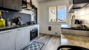 A modern kitchen with grey cabinets, a built-in oven, and a window with a view of the outside. - (033) Le sunny & cosy city trip (Antibes)