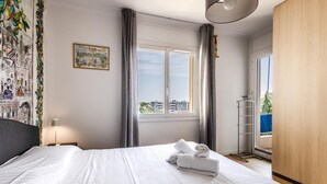 A hotel room with a large bed, a window with curtains, a painting on the wall, and a wooden wardrobe. - (033) Le sunny & cosy city trip (Antibes)