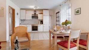Una cucina moderna con mobili bianchi, un'area pranzo con tavolo e sedie, e una sedia in vimini con una bottiglia e un bicchiere.