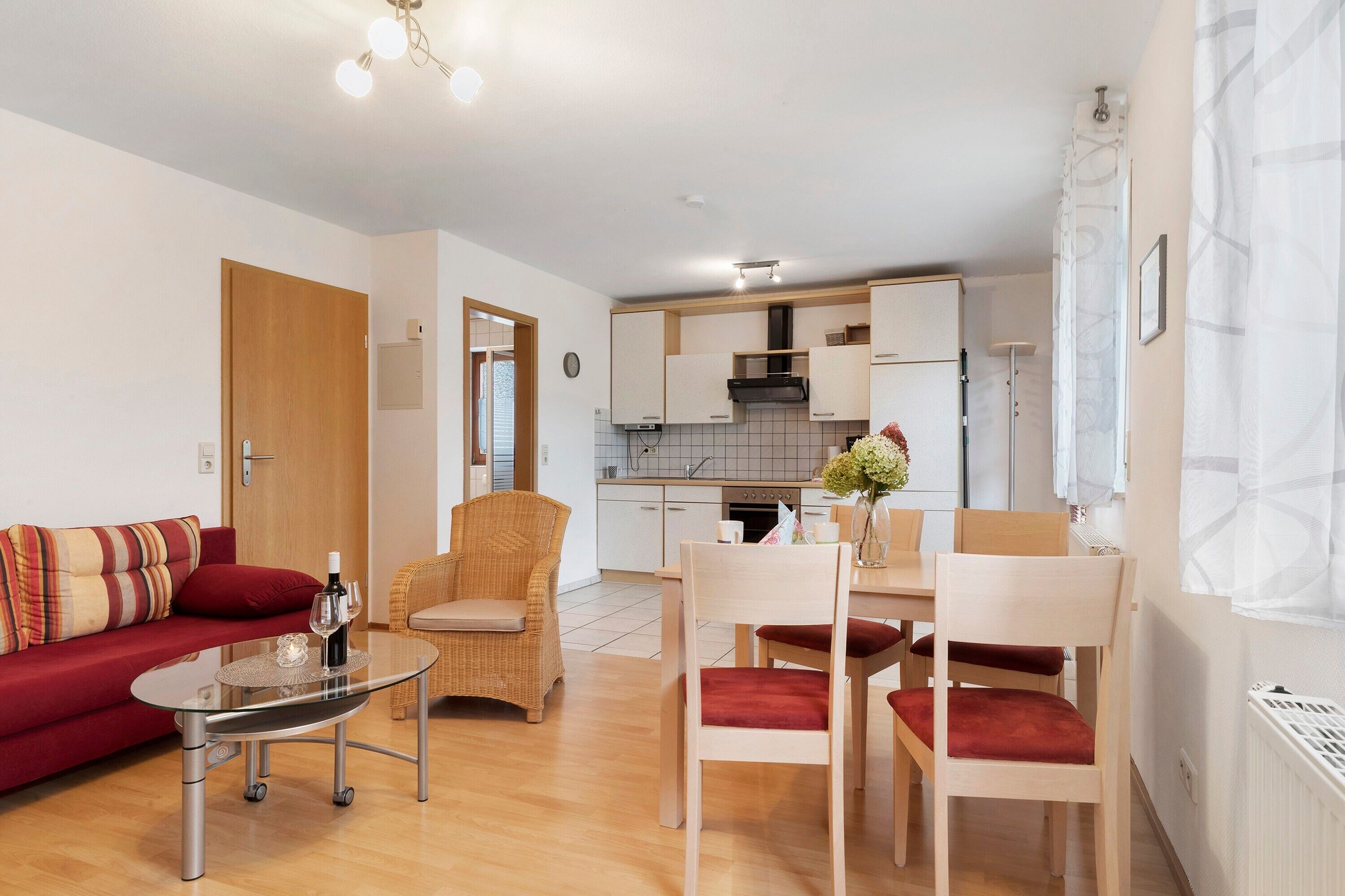 A modern living room with a sofa, chairs, a glass table, and a kitchen in the background.