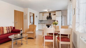 Un soggiorno moderno con divano, poltrone, un tavolo in vetro e una cucina sullo sfondo.