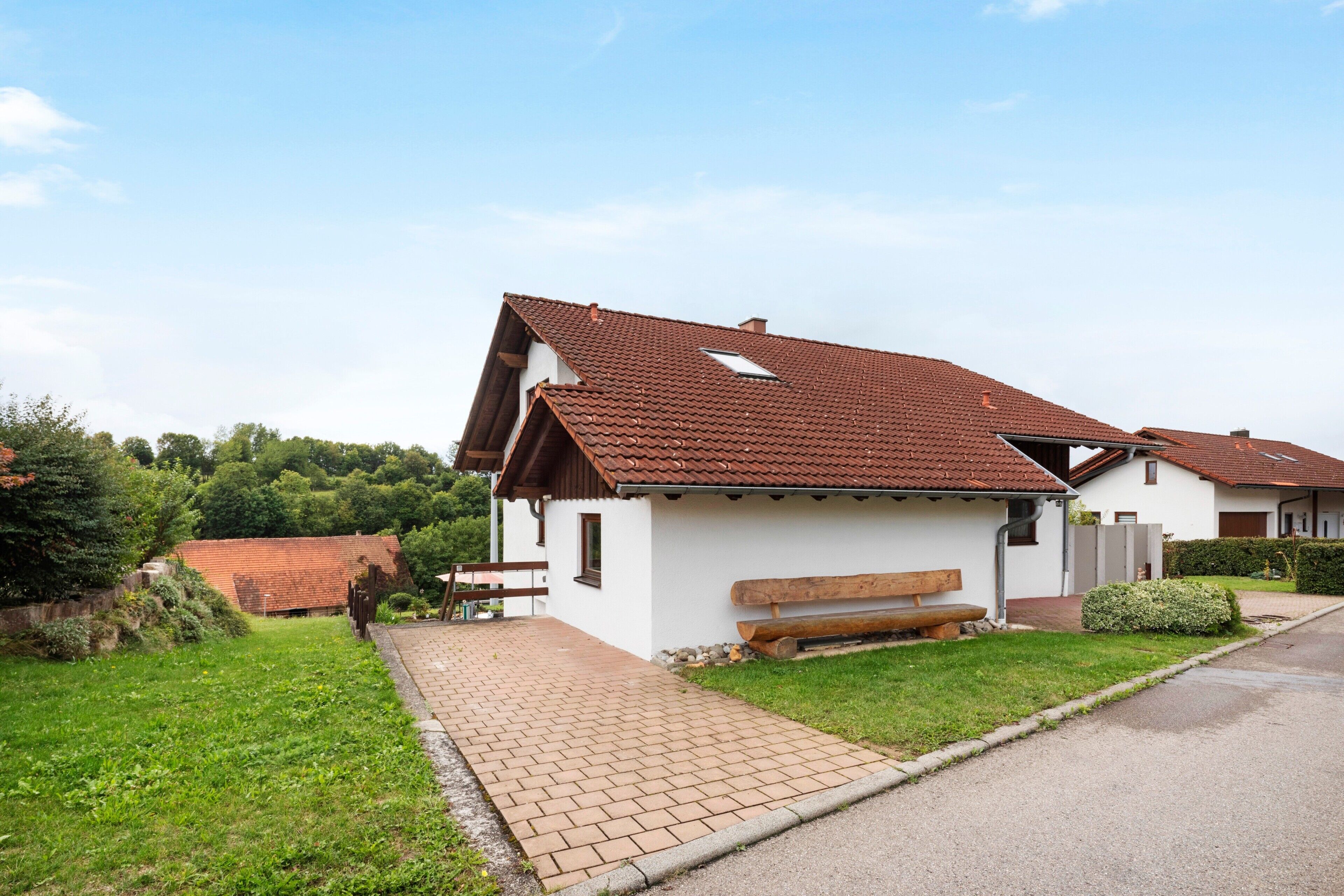 A residential building with a sloped roof, a paved driveway, and a bench outside.